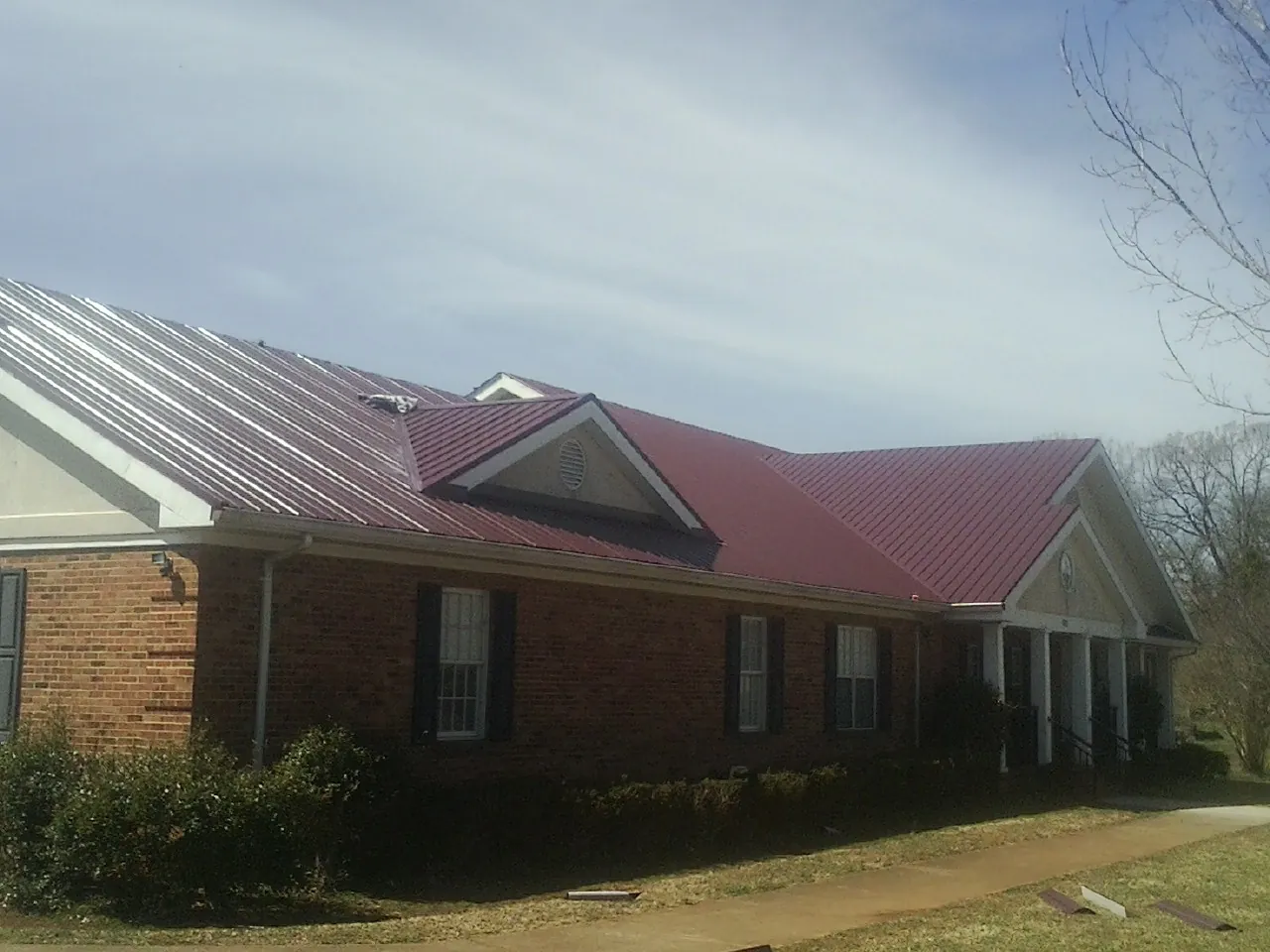 Red metal roof with gabled entries on a long brick building, from a Hail Damage Roof Repair job in Capistrano Beach